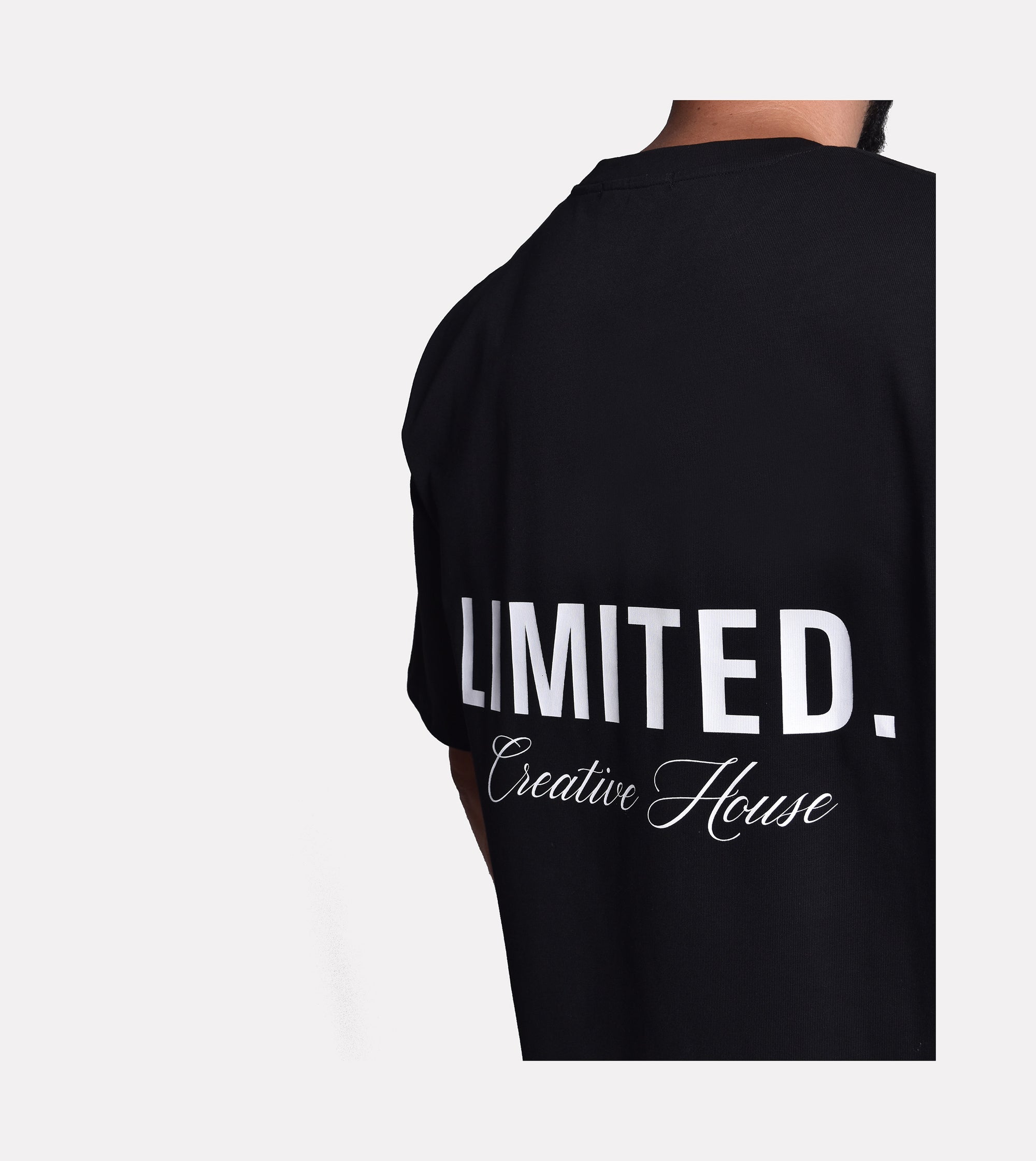 Close-up of model wearing LIMITED. Oversized mens t-shirt back view in black with big white LIMITED. branding on the back.