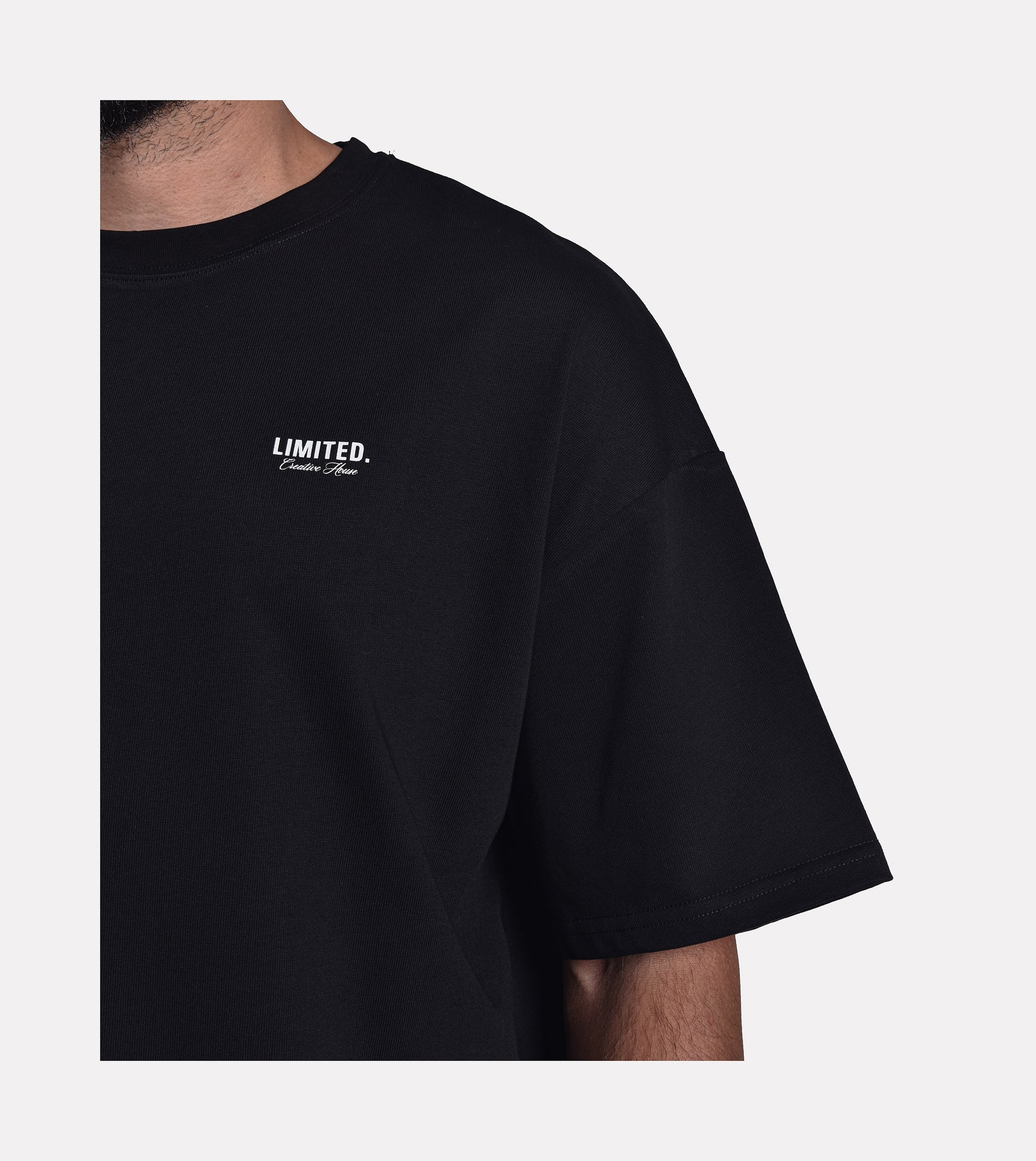 Close-up of model wearing LIMITED. Oversized mens t-shirt front view in black with white small branding on the left chest.