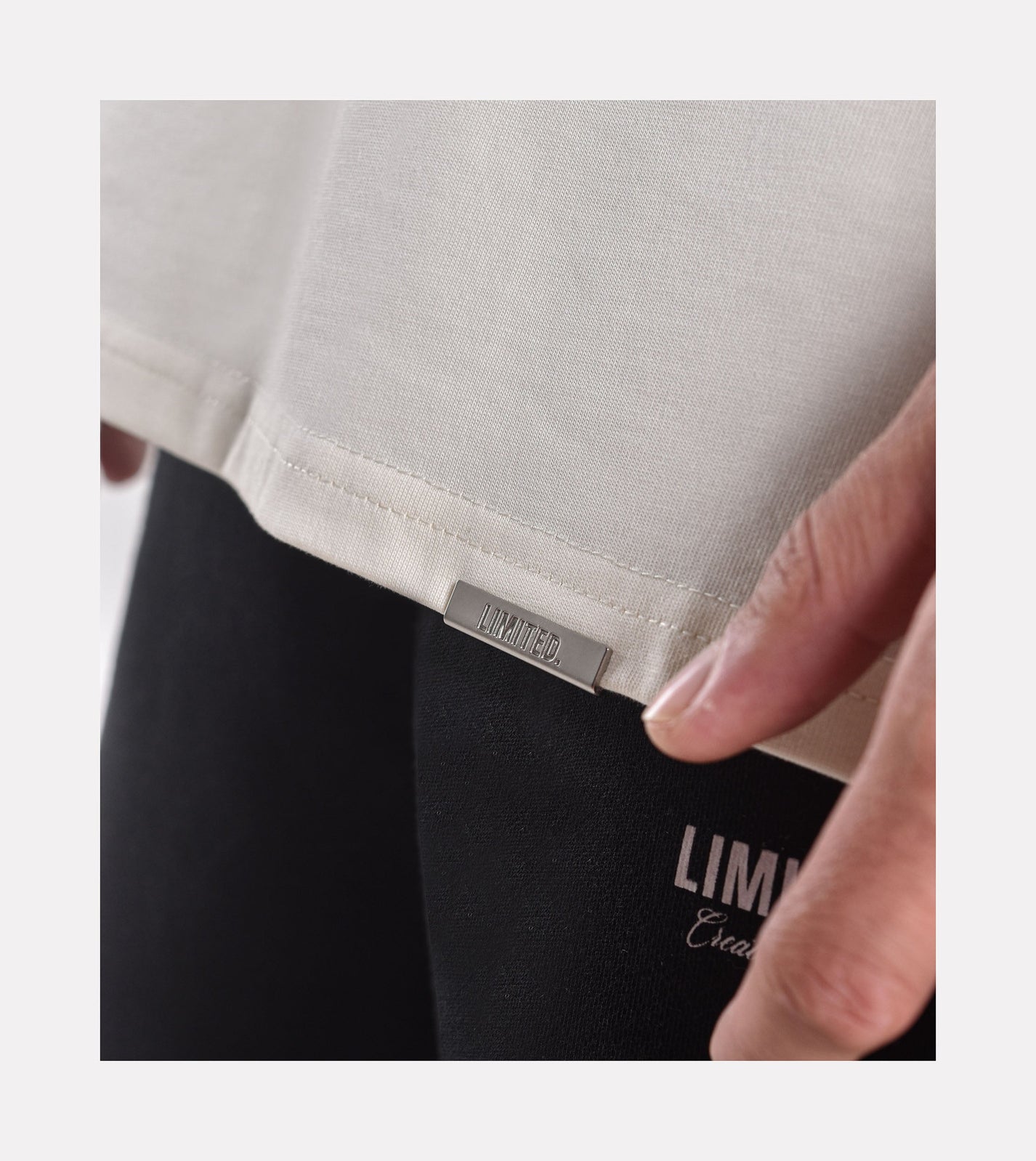 Close-up of model wearing LIMITED. Oversized mens t-shirt front view in off-white colour with signature metal branding to the hem.