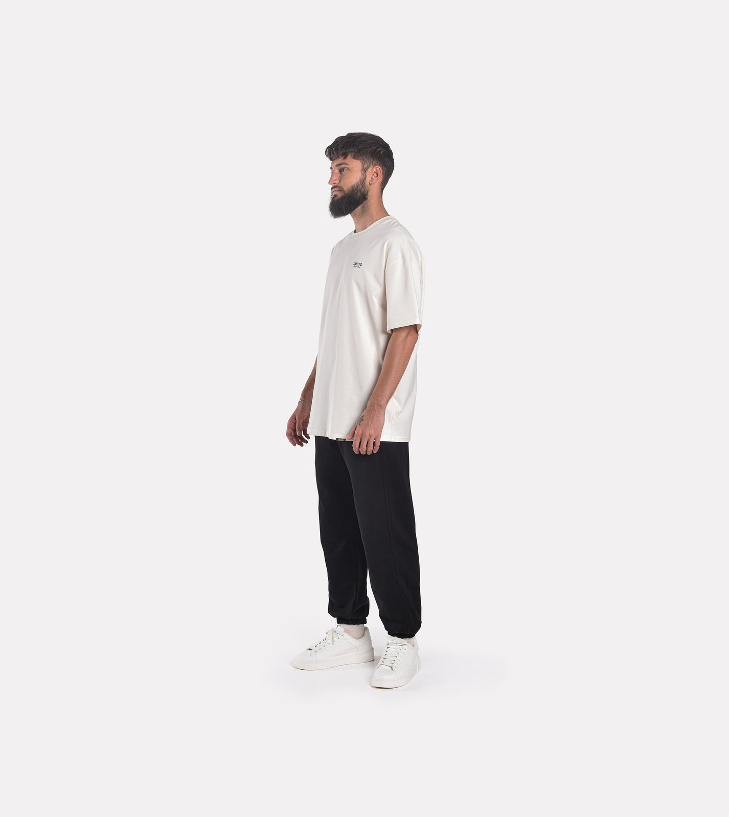 Side-view of model wearing LIMITED. Oversized mens t-shirt in off-white colour with small black branding on the left chest.